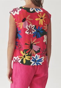 Hemd mit Blumenmuster auf rosa Hintergrund, das mehrfarbige Blumen in verschiedenen Formen zeigt. Kombiniert mit einfarbigen rosa Hosen.