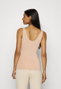 Jasnoróżowy top na ramiączkach z głębokim wycięciem na plecach. Miękka, elastyczna tkanina z minimalną ilością szwów, dopasowany krój. Noszony z spodniami w kolorze skóry, prezentującymi prosty design.