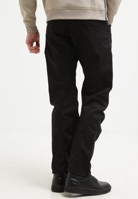 Svarta byxor med rak passform, gjorda av lätt tyg, i kombination med texturerade svarta sneakers. Enkelt utförande, inga synliga mönster.