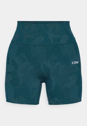 Shorts de cyclisme taille haute en teal fabriqués dans un tissu extensible, présentant un motif subtil et un petit logo blanc sur le côté gauche.