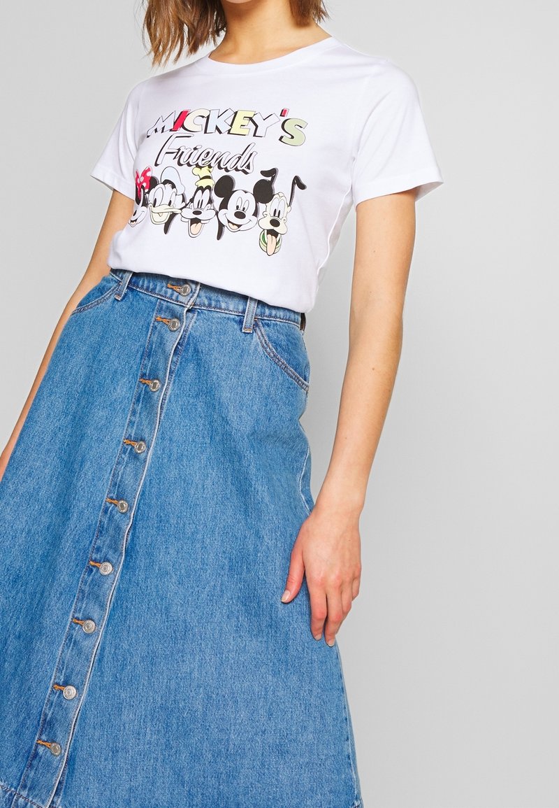 T-shirt blanc à manches courtes avec le texte "Les amis de Mickey" et des personnages, associé à une jupe en jean bleu taille haute avec boutons à l'avant.