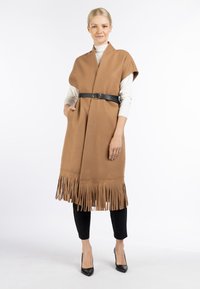 Kamelbrun poncho med frynser lavet af blødt stof, der er belted med et sort læderbælte; har en sjalkrave og sidelommer.