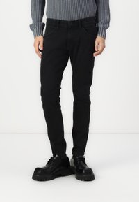 Černé džíny z denimu s přiléhavým střihem, které mají klasický pětikapsový design a zapínání na knoflík. Spárovány s masivními černými šněrovacími botami.