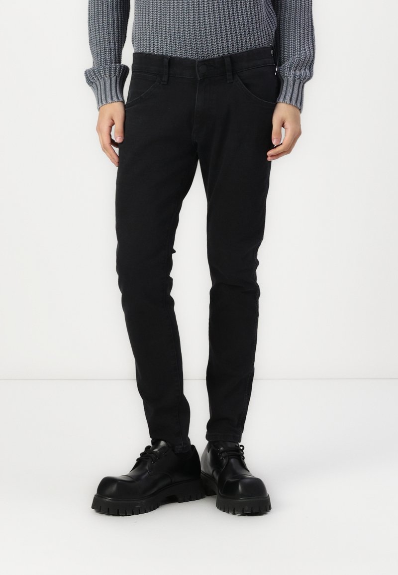 Černé džíny z denimu s přiléhavým střihem, které mají klasický pětikapsový design a zapínání na knoflík. Spárovány s masivními černými šněrovacími botami.