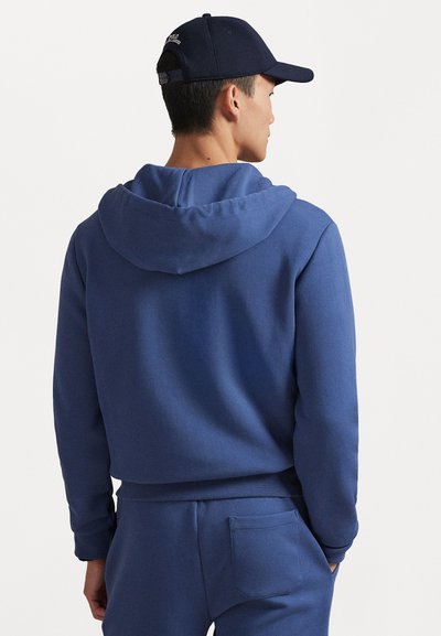 Zila kapuce ar aukliņu, izgatavota no mīksta auduma. Ir aļņu kabata un ribotas piedurknes, valkāta kopā ar saskaņotiem sporta biksēm un ķiveri.