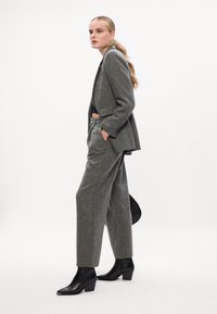 Fato cinza sob medida com um blazer estruturado e calças de perna larga, feito de um tecido texturizado. Combinado com botas de tornozelo pretas.