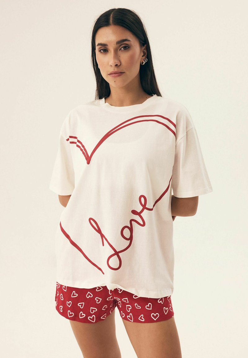 Biała bawełniana koszulka z czerwonym sercem i napisem "Miłość" w kursywie. Połączona z czerwonymi szortami w białe serca.