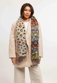 Luipaardprint sjaal met multicolor vlekken in tinten van bruin, groen, blauw en oranje; gefranjerde randen; gedragen over een gestructureerde beige jas.