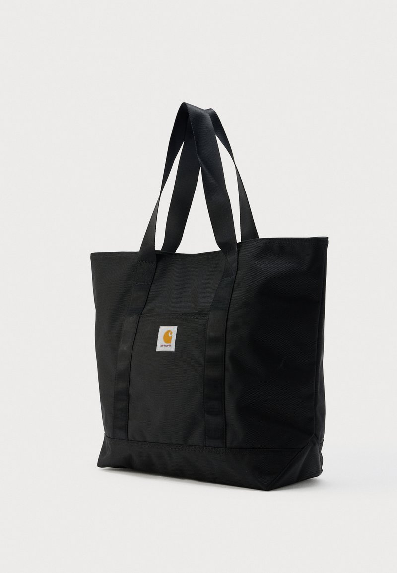 Borsa tote Carhartt nera con doppie cinghie per la spalla e toppa frontale con logo su sfondo chiaro e uniforme.