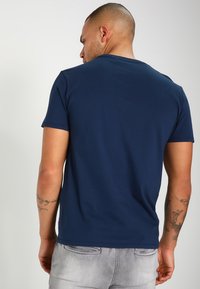 Camiseta azul marino de algodón suave con cuello redondo y mangas cortas; textura lisa y diseño ajustado, vista desde la parte posterior.