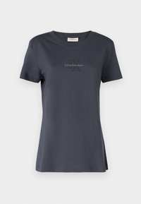 Tmavě šedé tričko s krátkým rukávem vyrobené z měkké bavlněné látky. Má kulatý výstřih a nenápadné logo Calvin Klein Jeans na hrudi.