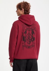 Sudadera color burdeos con un gran diseño gr�áfico negro que presenta una calavera y una espada, decorada con alas de murciélago, y con capucha ajustable.