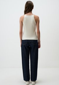 Top a costine di colore crema con schiena alta e spalline larghe, abbinato a jeans a gamba larga di colore blu navy. Sneakers bianche in basso.