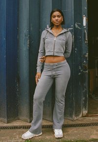 Grijze twee-delige trainingsoutfit van zachte stof, bestaande uit een crop hoodie en joggingsbroek met drawstring. Gecombineerd met witte sneakers.