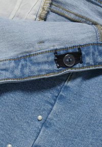 Lichtblau denim stof met een horizontale gestikte naad, met een knoopsluiting en kleine witte decoratieve parels op de stof.