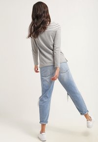 Haut à manches longues rayé gris associé à un jean déchiré bleu clair. Le mannequin porte des baskets blanches. Tenue décontractée vue de l'arrière.