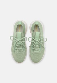 Baskets en tissu tricoté vert clair avec semelles blanches, lacets noués en nœuds et languettes à tirer sur la languette et le talon, vues de dessus.