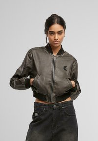 Tumedast hall nahk bomberjope, millel on ribitud krae ja mansetid, eesneel ja küljetaskud. Tikkitud logo detail rinnal.