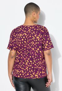 Camiseta de manga corta en tela morada con un estampado de leopardo en naranja y negro. Presenta un corte relajado y un escote redondo, combinada con leggings negros.