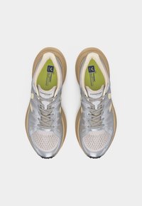 Ζευγάρι αθλητικά παπούτσια σε γκρι και μπεζ χρώμα με πάνω μέρος από δίχτυ και πράσινες εσωτερικές σόλες, φωτογραφημένα από πάνω σε λευκό φόντο.