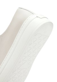 Close-up van een witte sneakers met een gestructureerde rubberen zool en een glad leren bovenwerk met gedetailleerde stiksels.