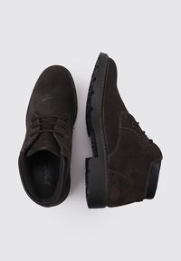 Botas de tobillo de ante marrón oscuro con cordones y suelas de goma negra, mostradas desde ángulos superiores y laterales sobre un fondo claro.