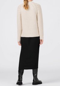 Krämfärgad ribbad stickad tröja med långa ärmar, matchad med en svart midi-kjol och svarta knähöga stövlar; minimalistisk design och neutrala färger.