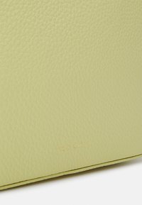 Limetkově zelená kožená taška s texturou kuliček; má vyražené logo ve zlatém písmu blízko spodní části; plochý design s čistými okraji.