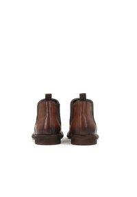 Botas de cuero marrón hasta el tobillo con lados elásticos, que presentan una textura suave y un tacón bajo apilado. Incluyen una lengüeta en la parte trasera.