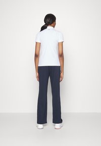 Hvit polo-skjorte med korte ermer og krage, kombinert med marineblå vide bukser. Outfiten fullføres med hvite sko.