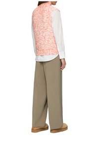 Gebreid vest in lichtoranje met gestructureerde textuur, gecombineerd met een wit shirt, losse khaki broek en tan slippers. Achteraanzicht.