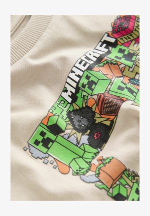 Beige pamut póló, színes Minecraft grafikával, zöld blokkokkal, karakterekkel és különböző játék szimbólumokkal. Simább textúra.