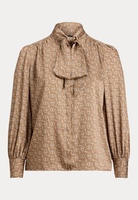 Bluse i lys brun stoff med geometriske mønstre i krem og oransje. Har høy krage med knytebånd og voluminøse ermer.