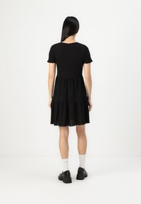 Black dress with short sleeves, tiered skirt, and scalloped hem. Made of lightweight fabric, features a simple round neckline and relaxed fit.