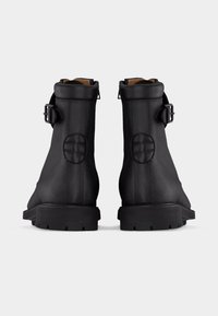 Paire de bottines en cuir noir avec semelles épaisses, col rembourré, boucles latérales et patchs circulaires cousus sur la zone du talon.