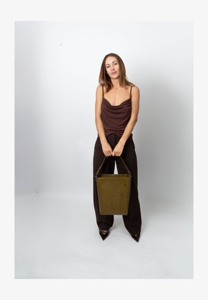 Borsa color verde oliva con motivo a coccodrillo e tracolla corta. Il modello indossa un top marrone con collo a scialle e pantaloni larghi scuri, in piedi davanti a uno sfondo semplice.