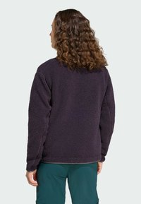 Giacca in pile viola con superficie morbida e strutturata, dotata di maniche lunghe e vestibilità ampia. Vista da dietro, senza elementi metallici visibili.