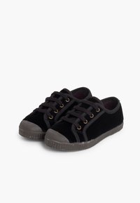 Un paio di sneaker nere basse con design a lacci, punte in gomma e suole in gomma testurizzata su uno sfondo neutro.