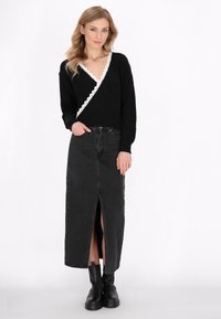 Maglione avvolgente nero con bordo scallop bianco, abbinato a una lunga gonna di jeans nera con spacco frontale e stivaletti neri alla caviglia.