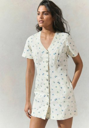 Robe florale blanche à manches courtes, avec un décolleté en V, fermeture à boutons et de petits motifs de fleurs bleues et vertes tout au long.