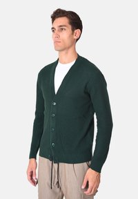 Cardigan verde scuro lavorato a maglia con scollo a V, cinque bottoni sul davanti, texture a costine e vestibilità comoda. Presenta maniche lunghe e orlo.