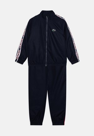 Takit ylös navy värit, jossa on vetoketjullinen takki ja elastiset hihansuut. Siinä on vaaleanpunaiset ja valkoiset raidalliset sivuaccentit sekä pieni vihreä logo rinnassa.