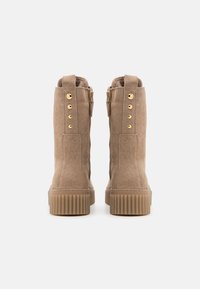 Tan nubuck ankelstøvler med en ribbet gummisål, baglynlås og hardware i guldfarve langs siden. Teksturér overflade.