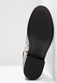 Semelle d'une bottine à motif peau de serpent noir et blanc montrant un talon en caoutchouc noir texturé et une semelle avec le nom de la marque ALDO.