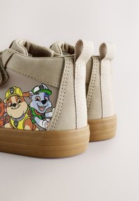 Béžové detské vysoké topánky s hnedými podrážkami a potlačenými postavičkami Paw Patrol na stranách, s textilnými pútkami na päte.
