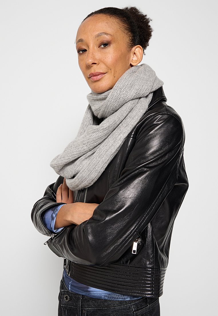 Bufanda gris hecha de un material suave y texturizado, envuelta de manera suelta, combinada con una chaqueta de cuero negra con acentos acanalados y un acabado liso.