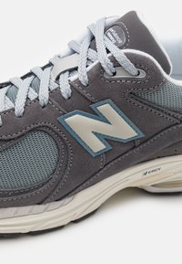 Herren-Laufschuh mit einem Obermaterial aus grauem Wildleder und Mesh, hellgrauen Schnürsenkeln, einem blauen Akzent-"N"-Logo und einer cremefarbenen Sohle mit strukturierten Details.