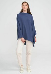 Navyblå poncho med avslappnad passform, tillverkad av mjukt tyg. Har en draperad design, långa ärmar och asymmetrisk fåll. Bärs med ljusa byxor.