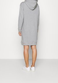 Vestido de sudadera de mezcla de algodón gris con mangas largas, puños y dobladillo acanalados, que presenta una capucha en la parte trasera. Se llevan zapatillas blancas en los pies.