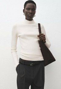 Top blanco de manga larga con cuello alto y textura acanalada, combinado con pantalones oscuros de corte ajustado y un bolso marrón de ante. Textura suave, silueta entallada.